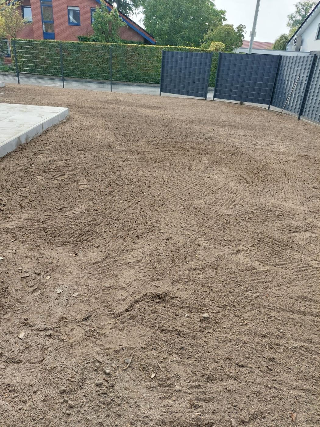 Planierte Erdfläche hinter einem Sichtschutzzaun, vorbereitet für neuen Rasen