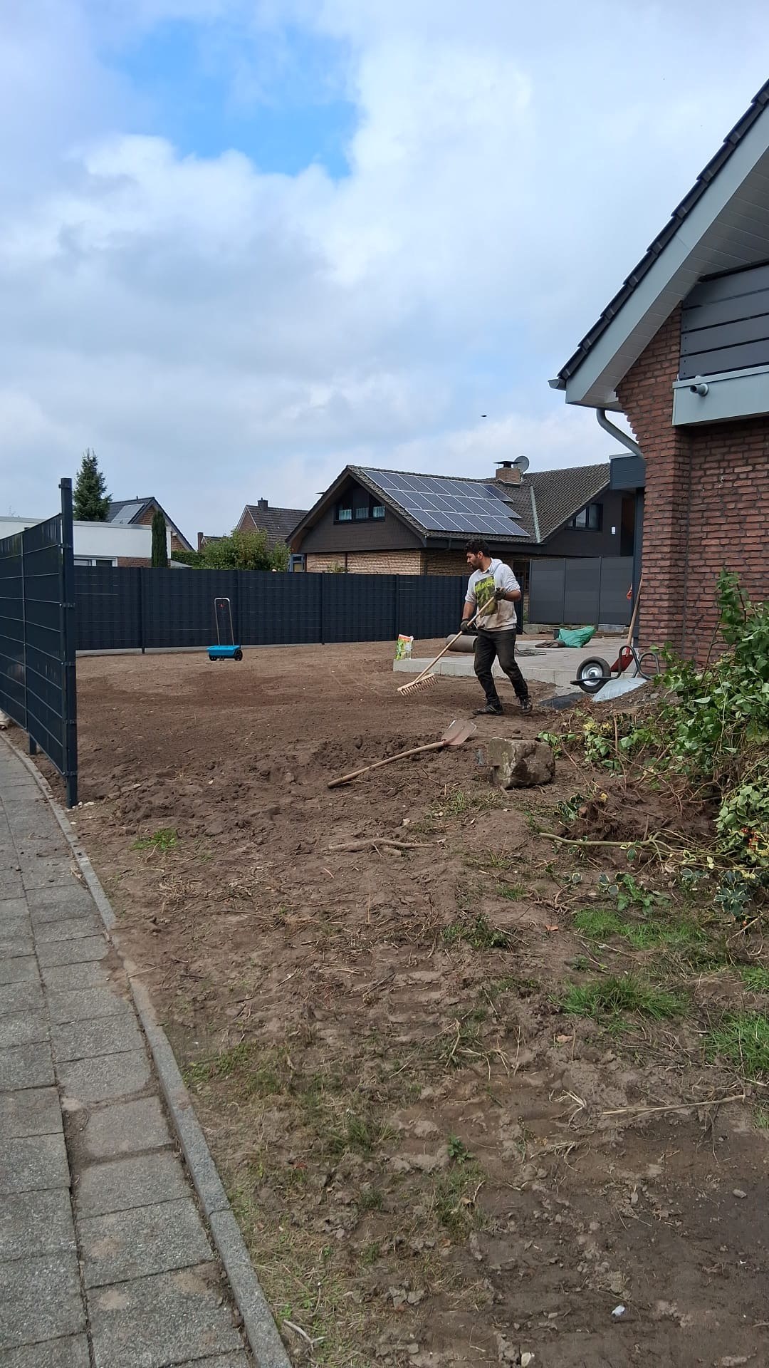 Gartenfläche an einem Wohnhaus wird mit dem Rechen für neuen Rasen vorbereitet
