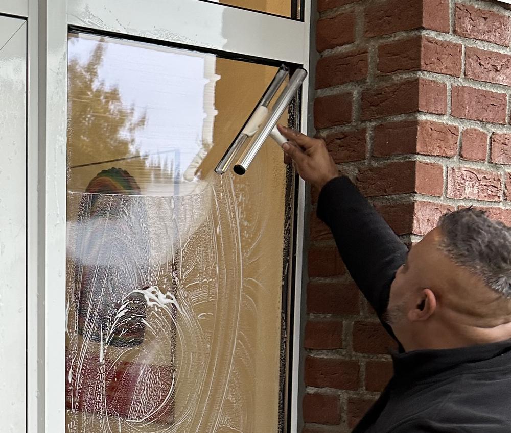 Mitarbeiter zieht eine Glasscheibe am Hauseingang mit dem Fensterwischer ab