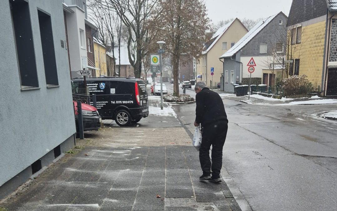 Mitarbeiter streut den Gehweg vor einer Häuserzeile ab